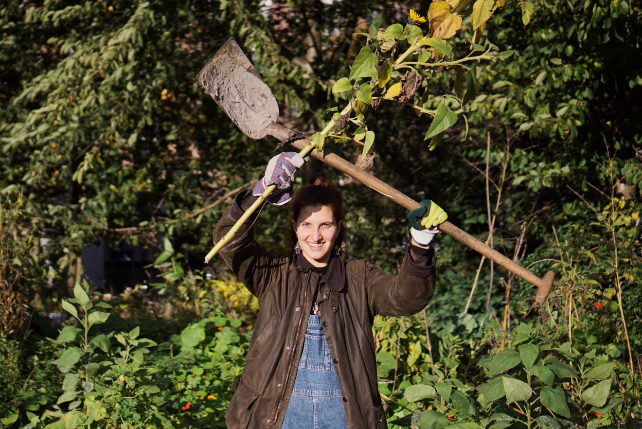 A woman holding a shovel and a sunflower stalk calling for good food and good farming